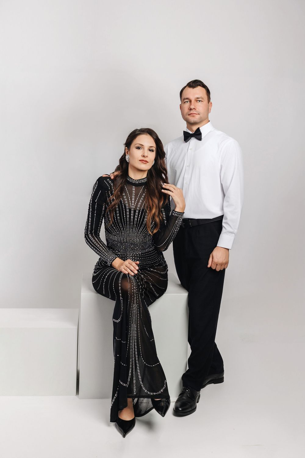 A couple poses together in formal attire against a white backdrop in a series of artistic studio photographs.