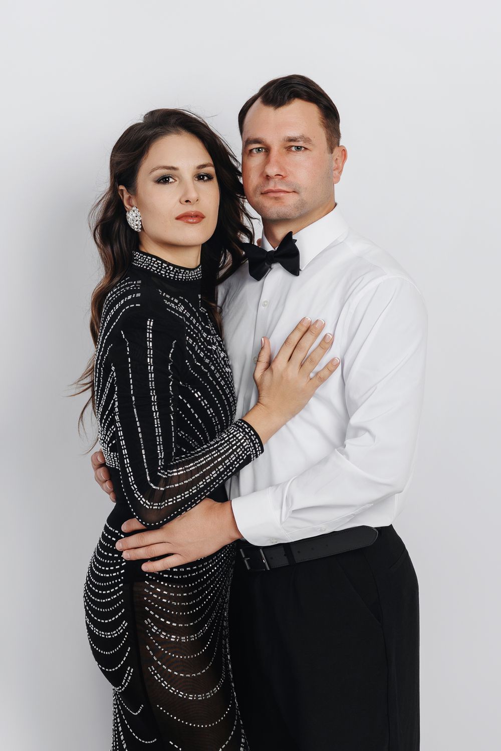 A couple poses intimately in formal attire against a white backdrop in a series of romantic portrait photos.