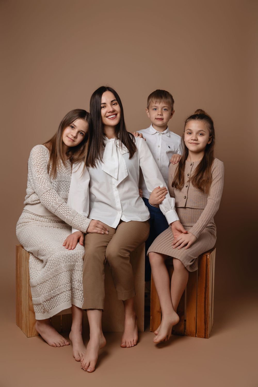 A group of four people wearing coordinated neutral-toned outfits pose together barefoot on a wooden bench for a portrait.