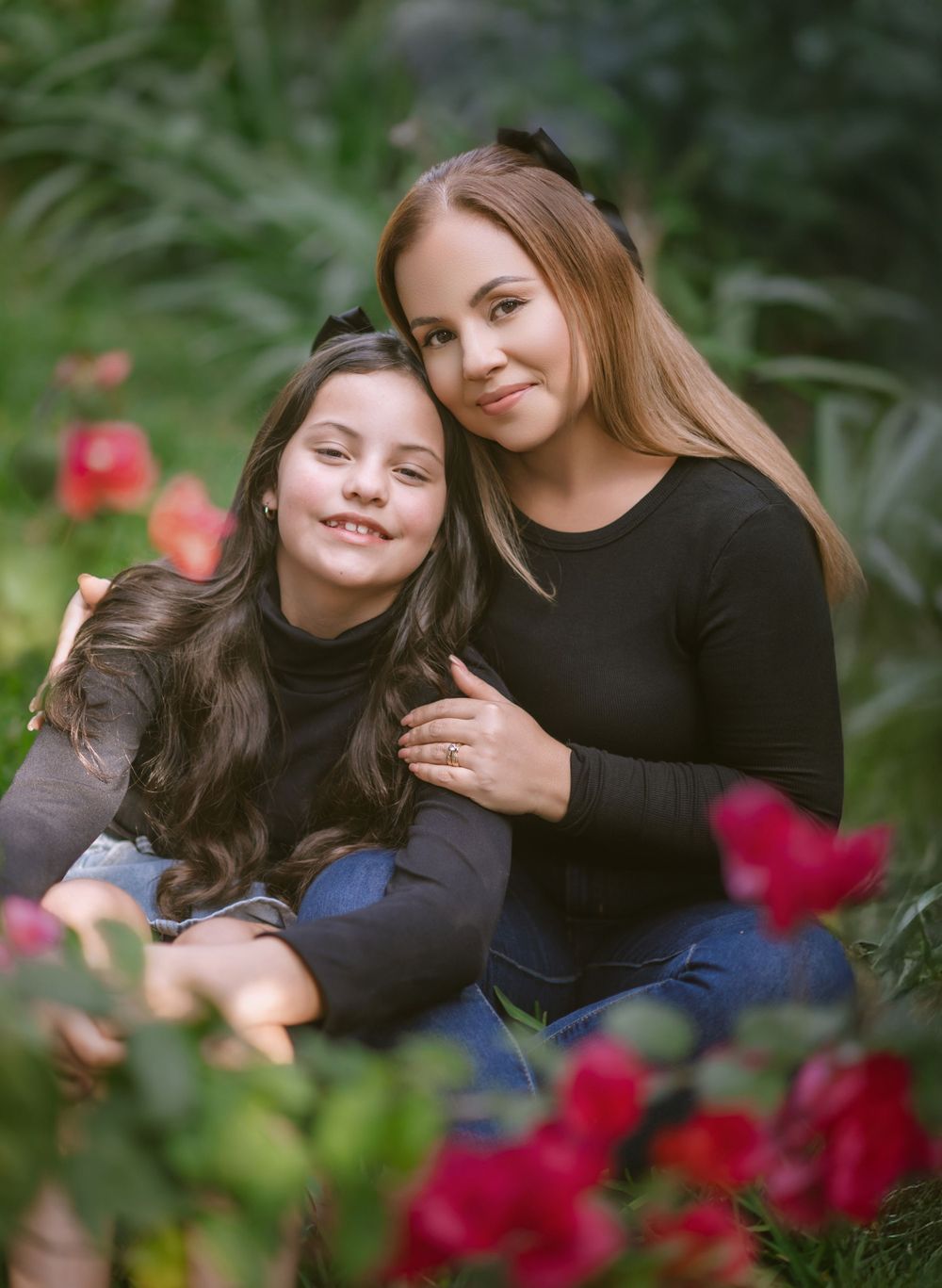 Two people sharing a tender moment together amid red roses and greenery in a garden setting.