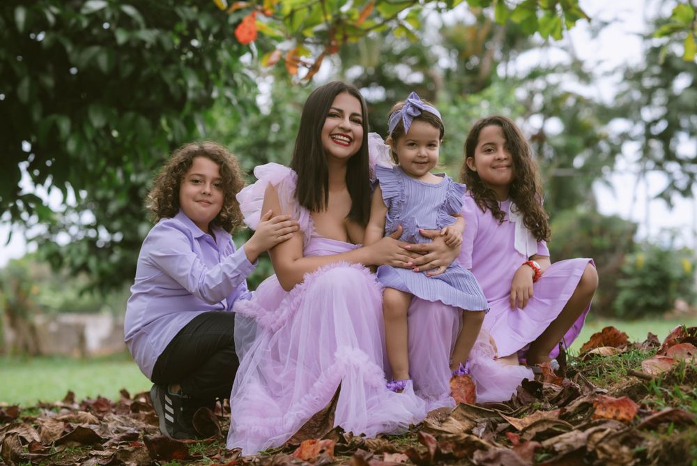 A family group wearing matching lavender outfits sits together on fallen autumn leaves in an outdoor setting.