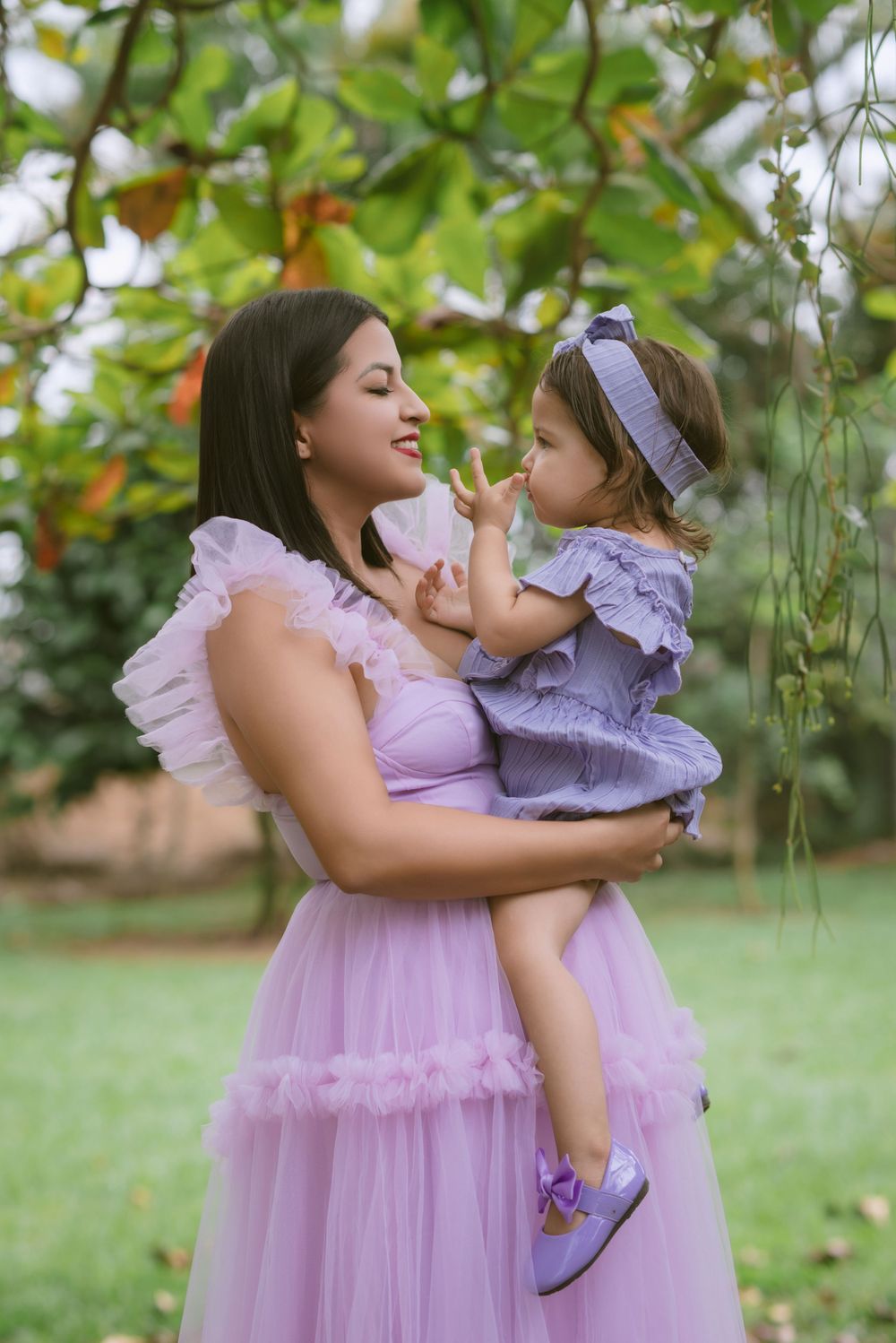 A tender moment between two people wearing matching lavender tulle dresses in a garden setting.