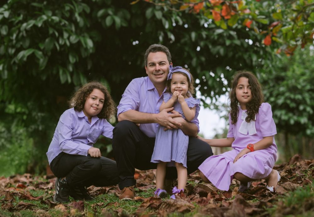 A group wearing lavender colored shirts sits together outdoors in a natural autumn setting with colorful foliage.