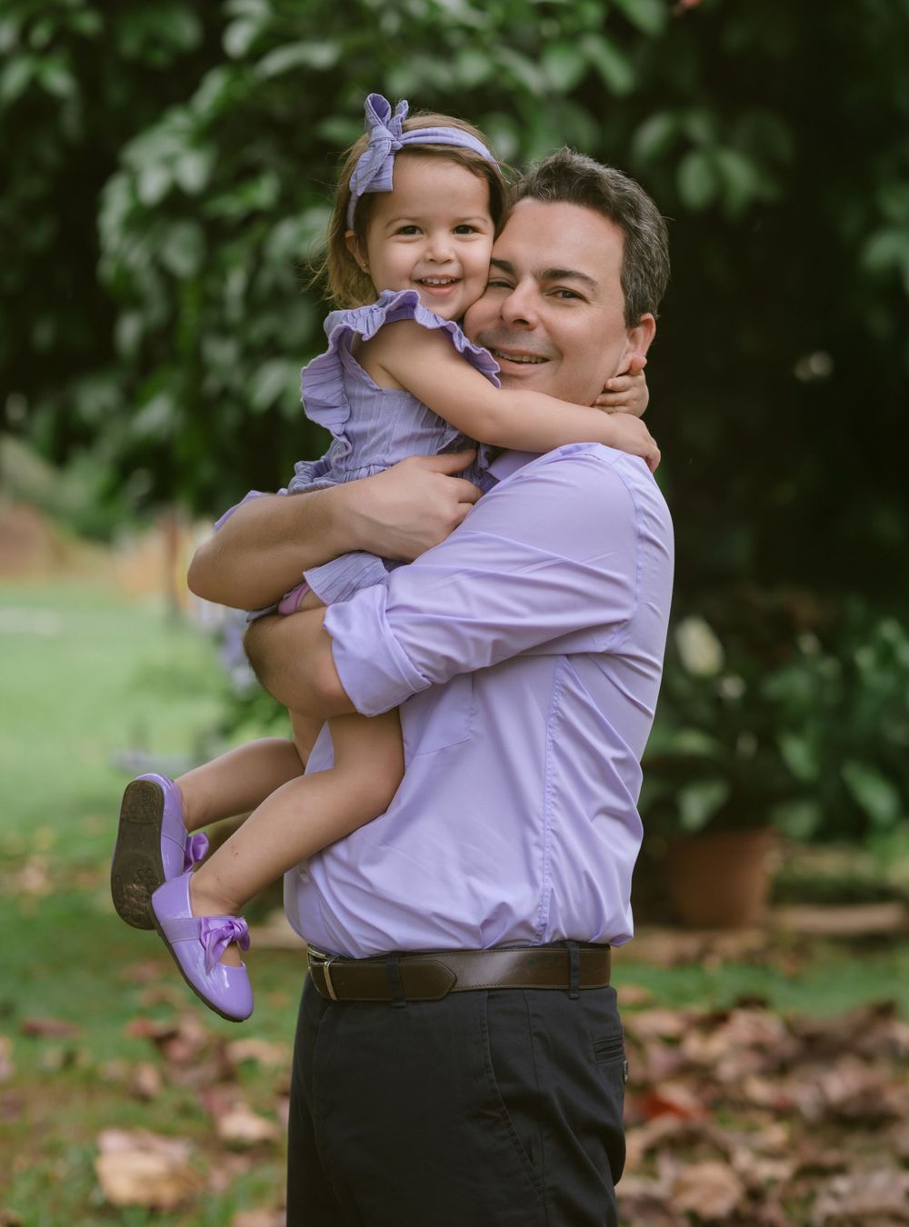A joyful moment captured outdoors as two people in purple attire share a warm embrace in a garden setting.