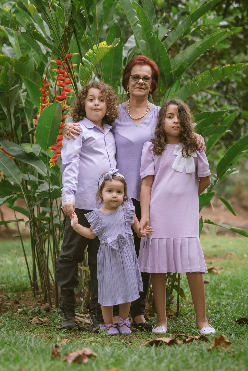 A family group poses together in a garden setting wearing coordinating lavender and purple outfits.