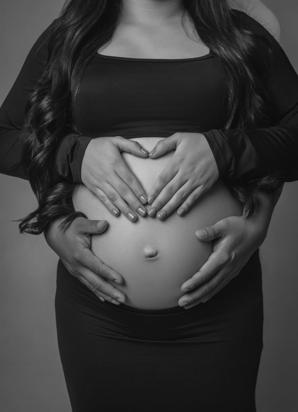 Black and white maternity photo showing hands forming heart shape on pregnant belly.