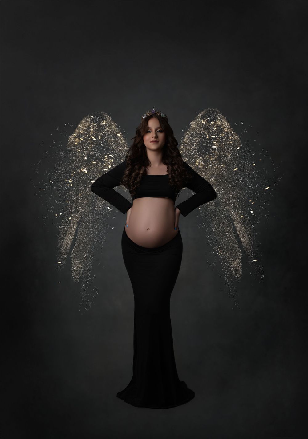 Artistic maternity photo with glowing angel wings effect against dark background.