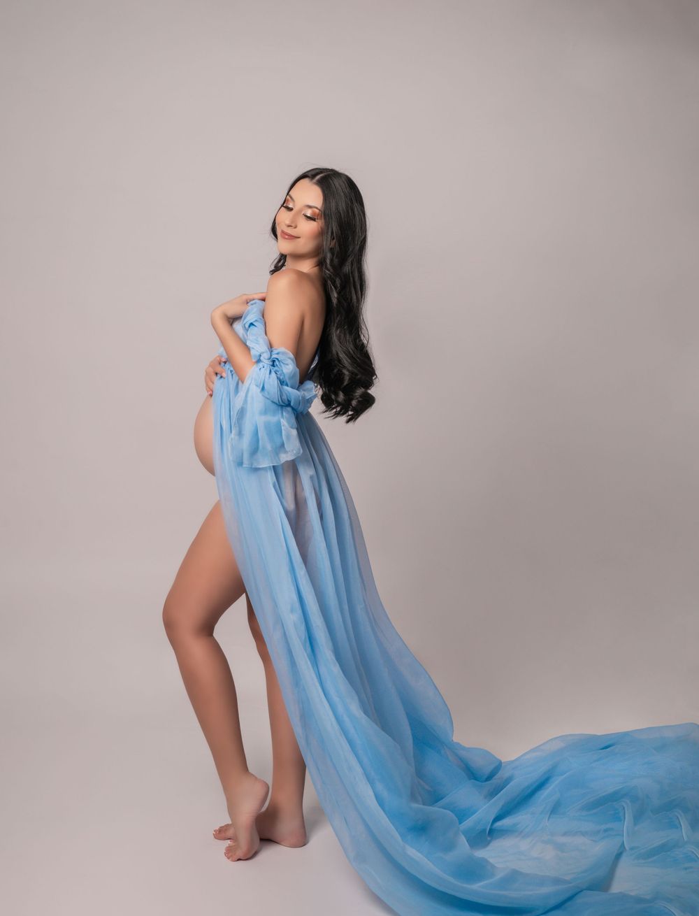 Graceful maternity portrait with billowing blue chiffon dress in studio setting.