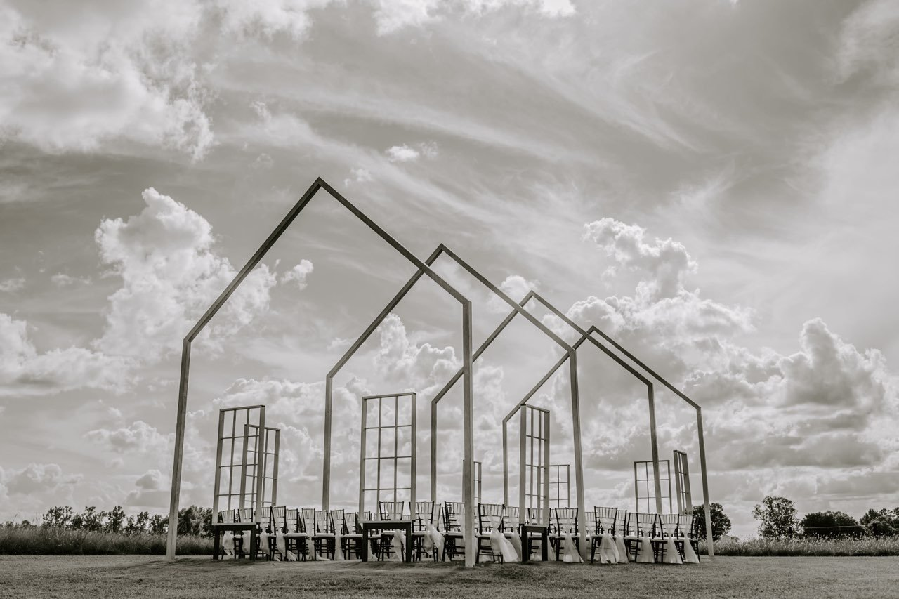 Minimalist outdoor chapel frames with geometric outlines against cloudy sky.