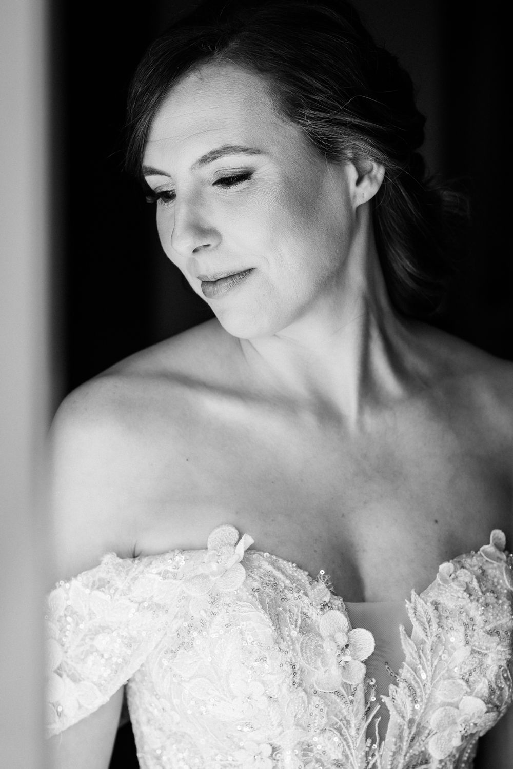 Black and white portrait of a bride in lace off-shoulder wedding dress looking to the side with delicate makeup.