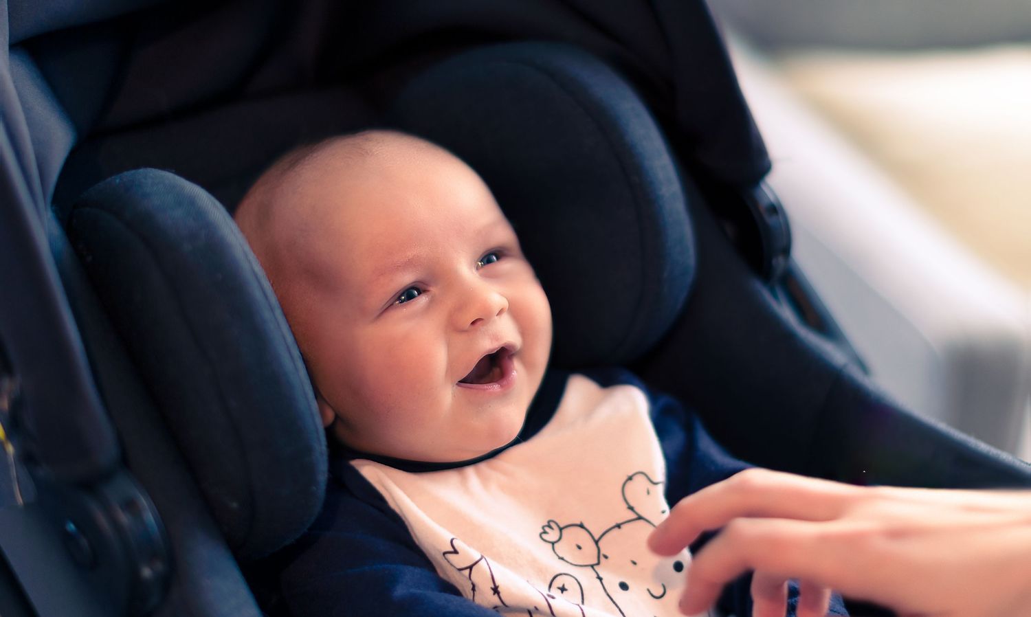 Smiling baby reclines in a navy blue car seat wearing a light colored outfit.
