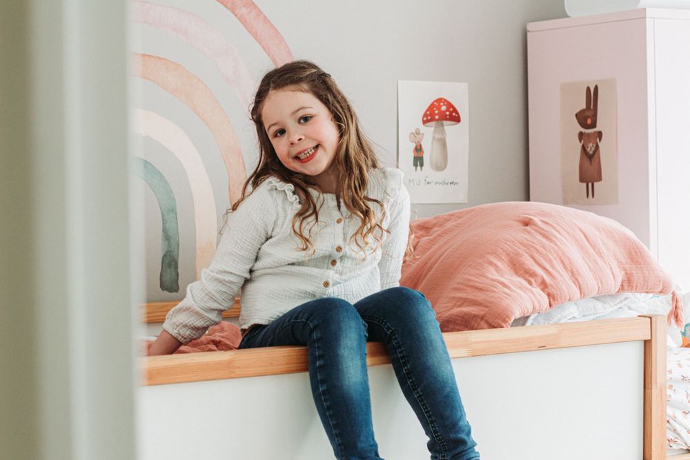 Petite fille au bord de son lit dans sa chambre d'enfant