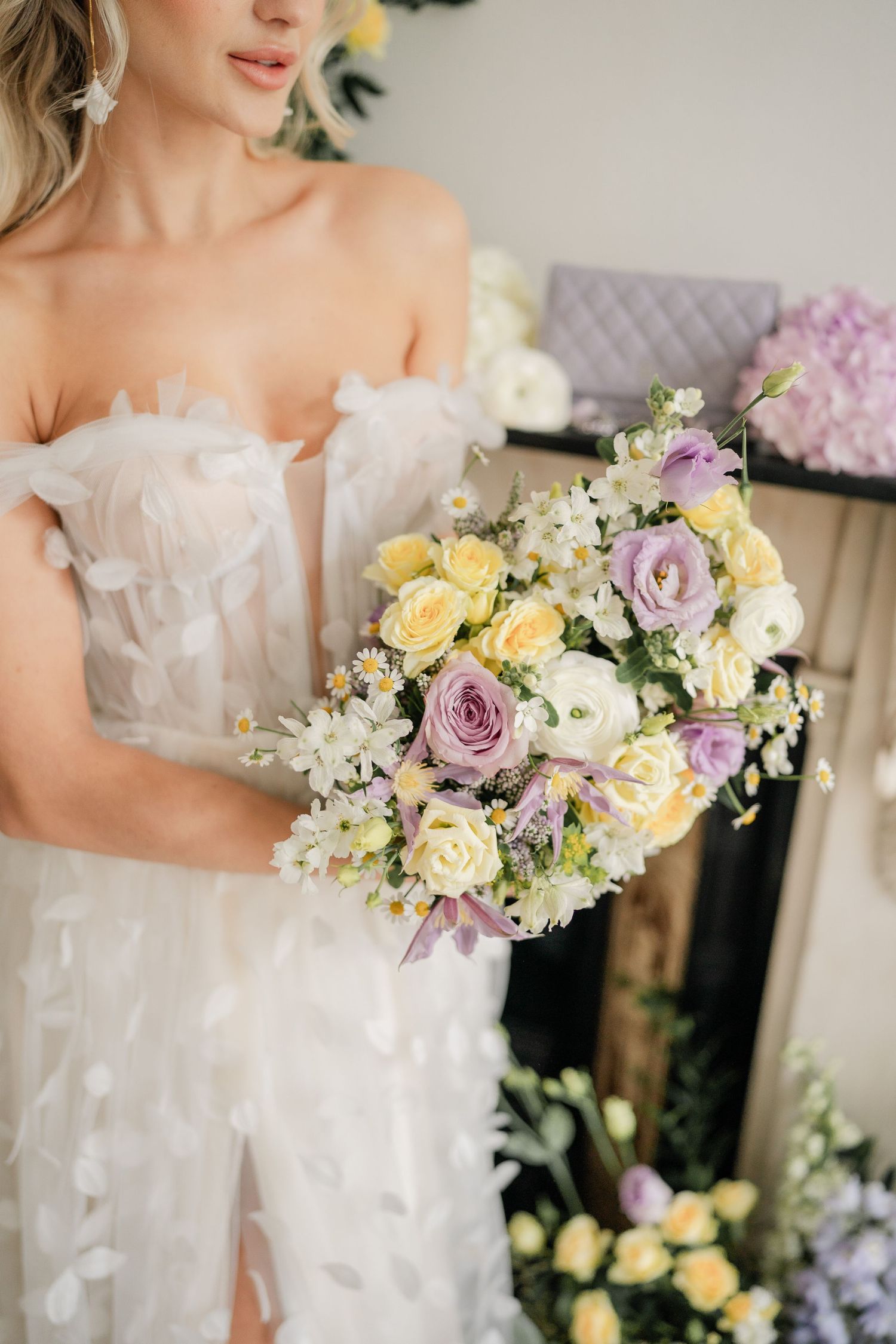 Close up of white textured wedding dress with pastel purple and yellow floral bouquet.
