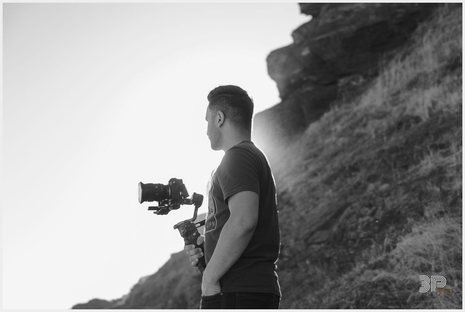 Silhouette of videographer with camera gear against mountainous backdrop.