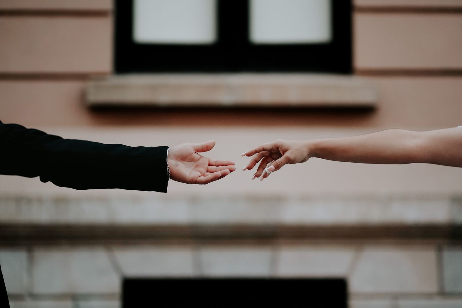 Two hands reaching toward each other against a building facade background.