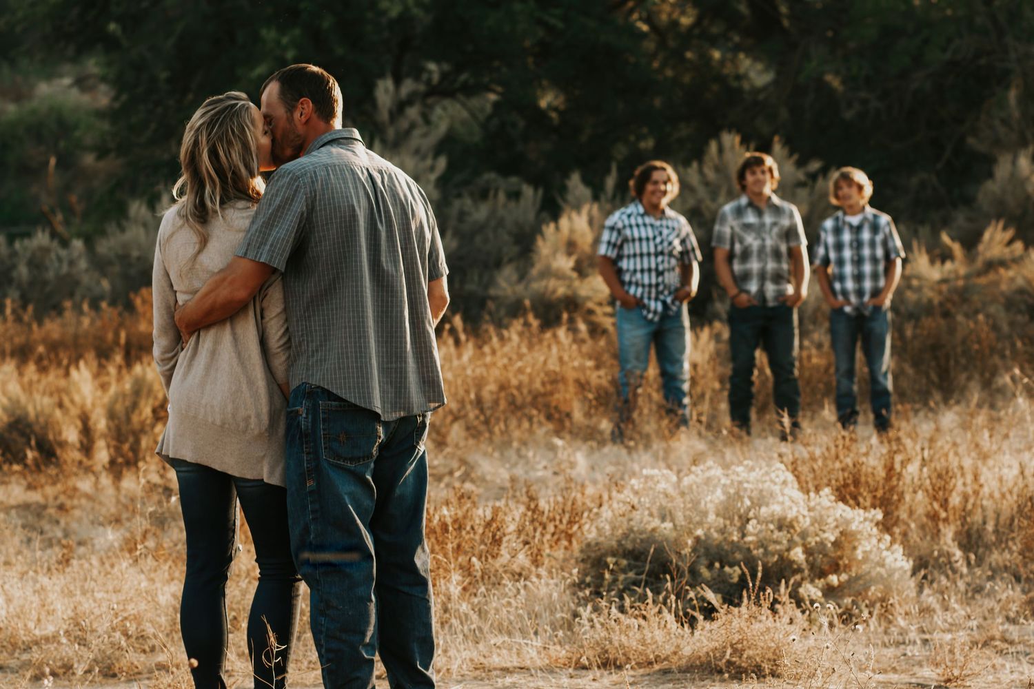 Mom and dad embracing in foreground with three sons in plaid shirts standing in background in Tri Cities, Washington.