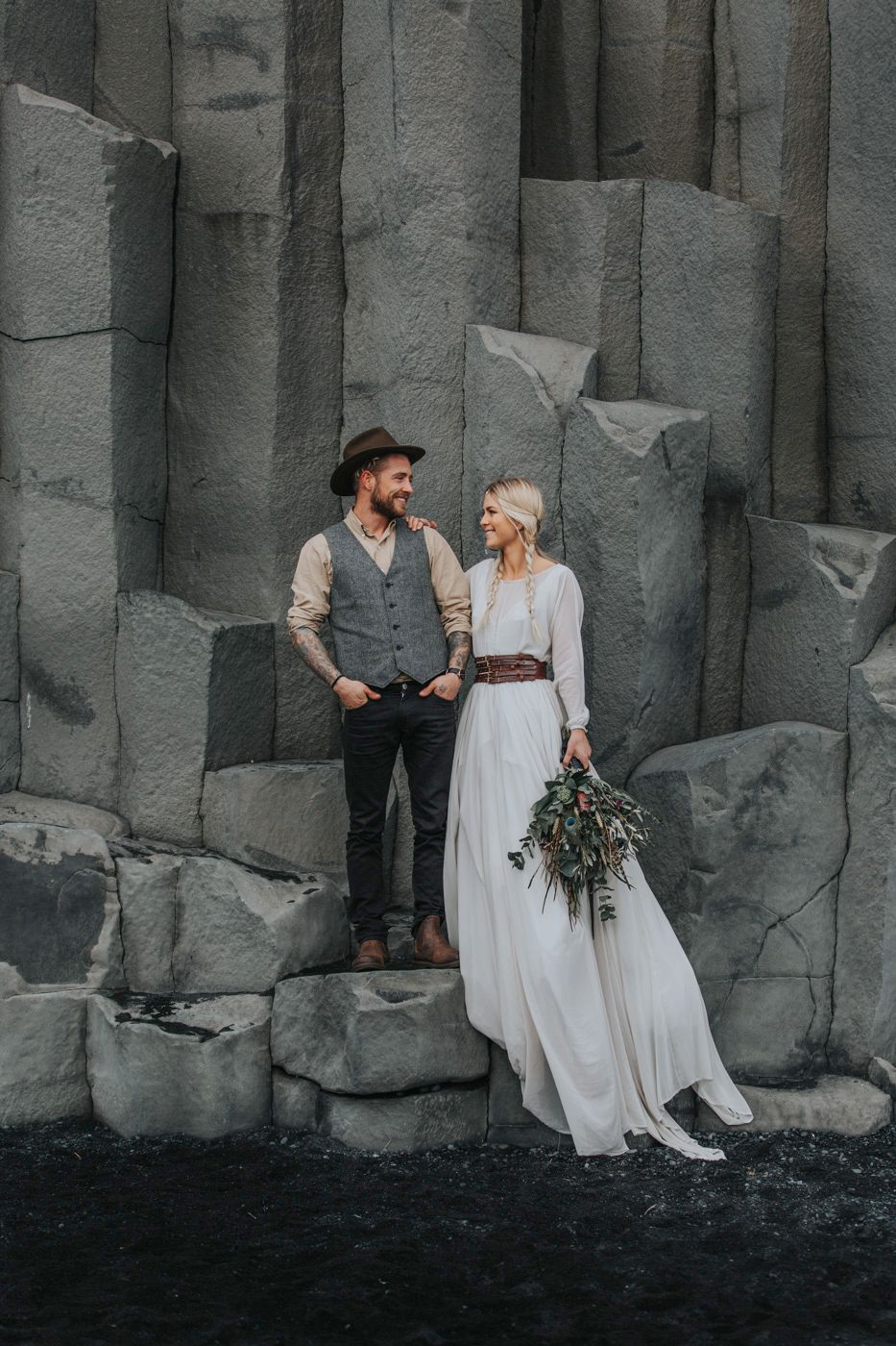 Wedding couple posing on geometric basalt rock formations by black sand beach.