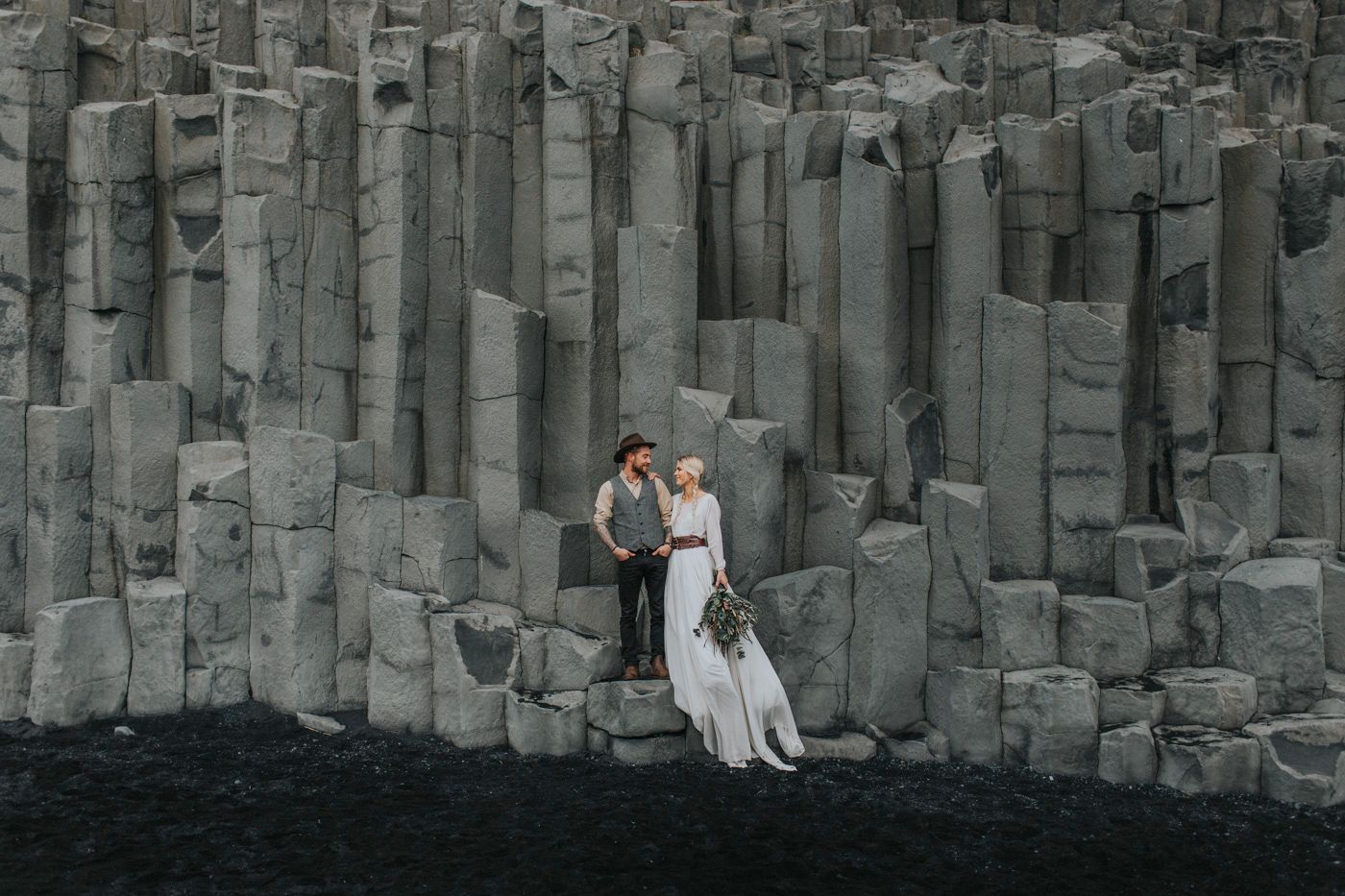 Wedding couple embracing against dramatic basalt column rock formation.