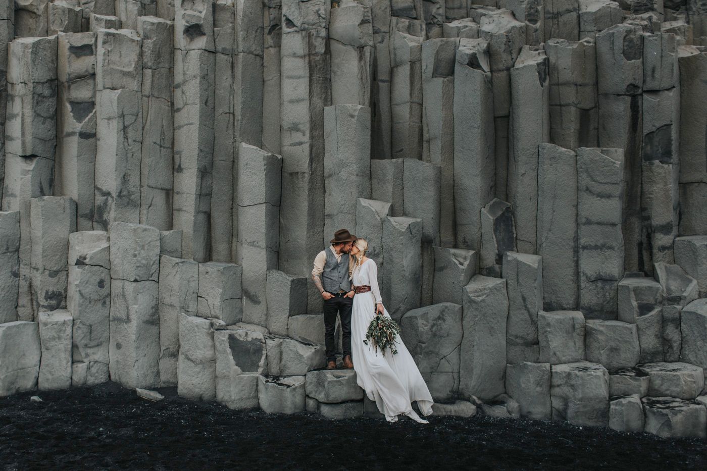 A romantic wedding portrait against dramatic basalt columnar rock formations on a black sand beach in Iceland.