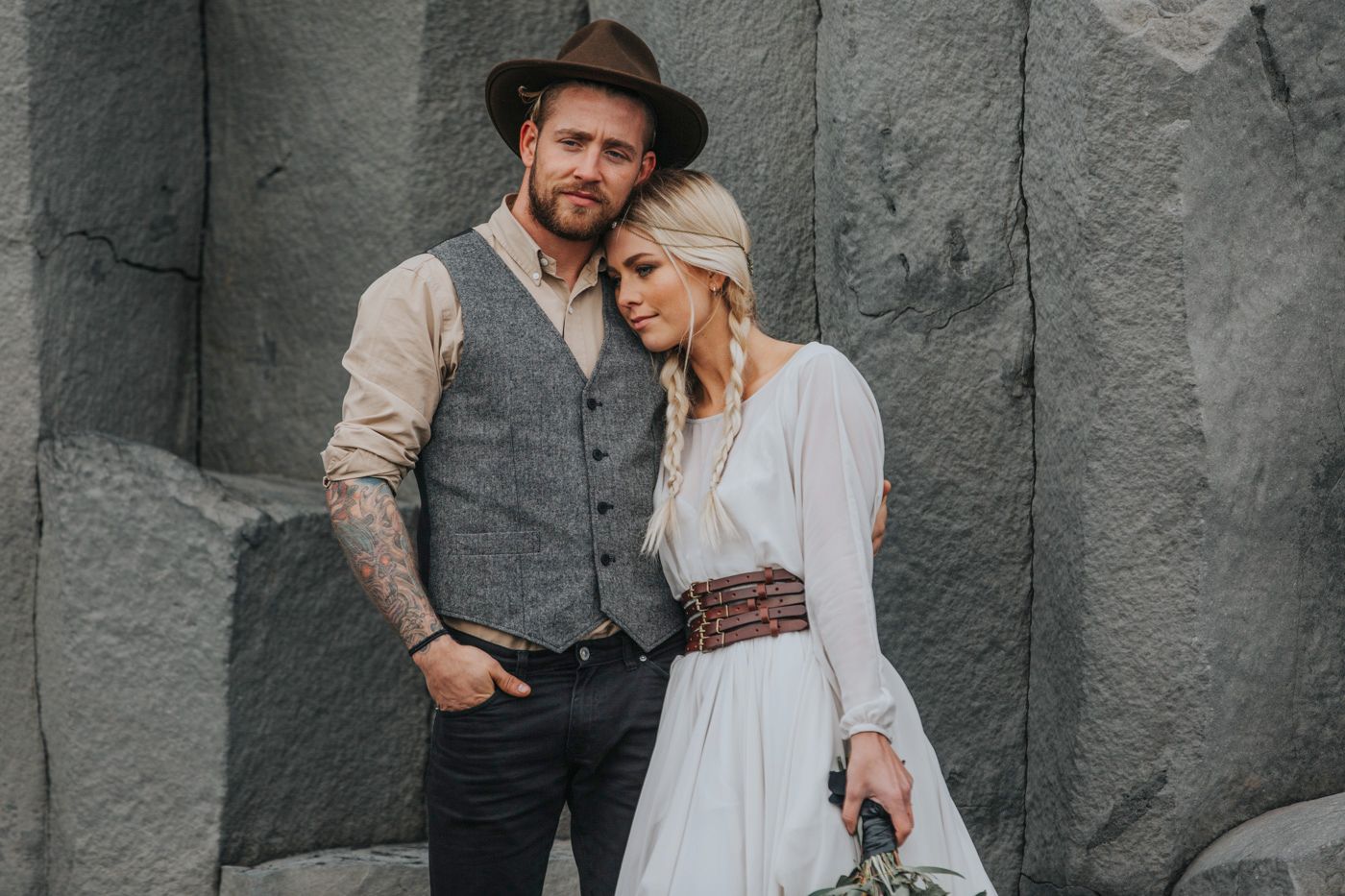 An intimate wedding portrait featuring rustic attire against dramatic volcanic rock formations.