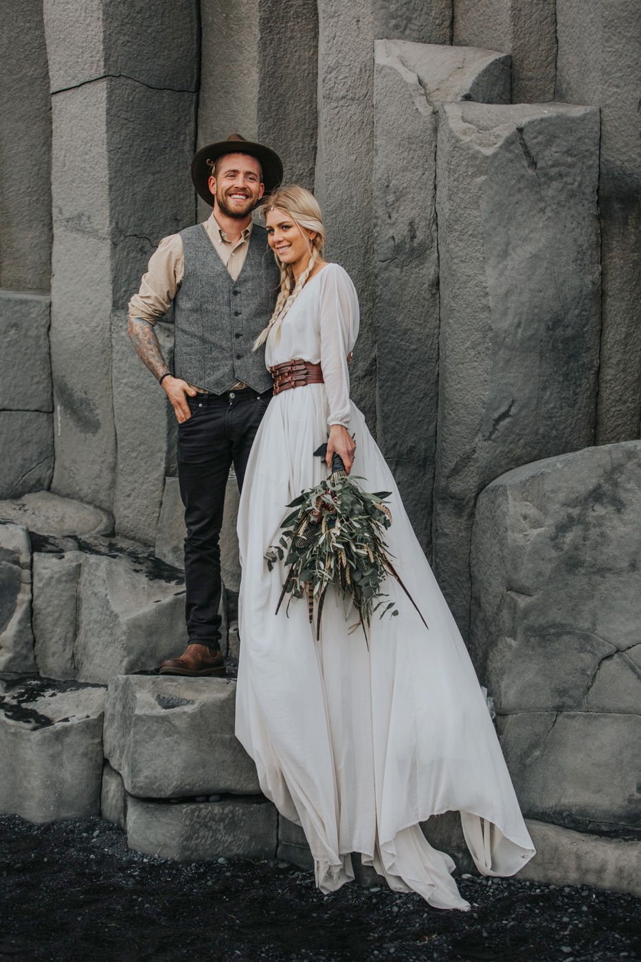 A stylish couple in western-inspired wedding attire standing on basalt rock formations.