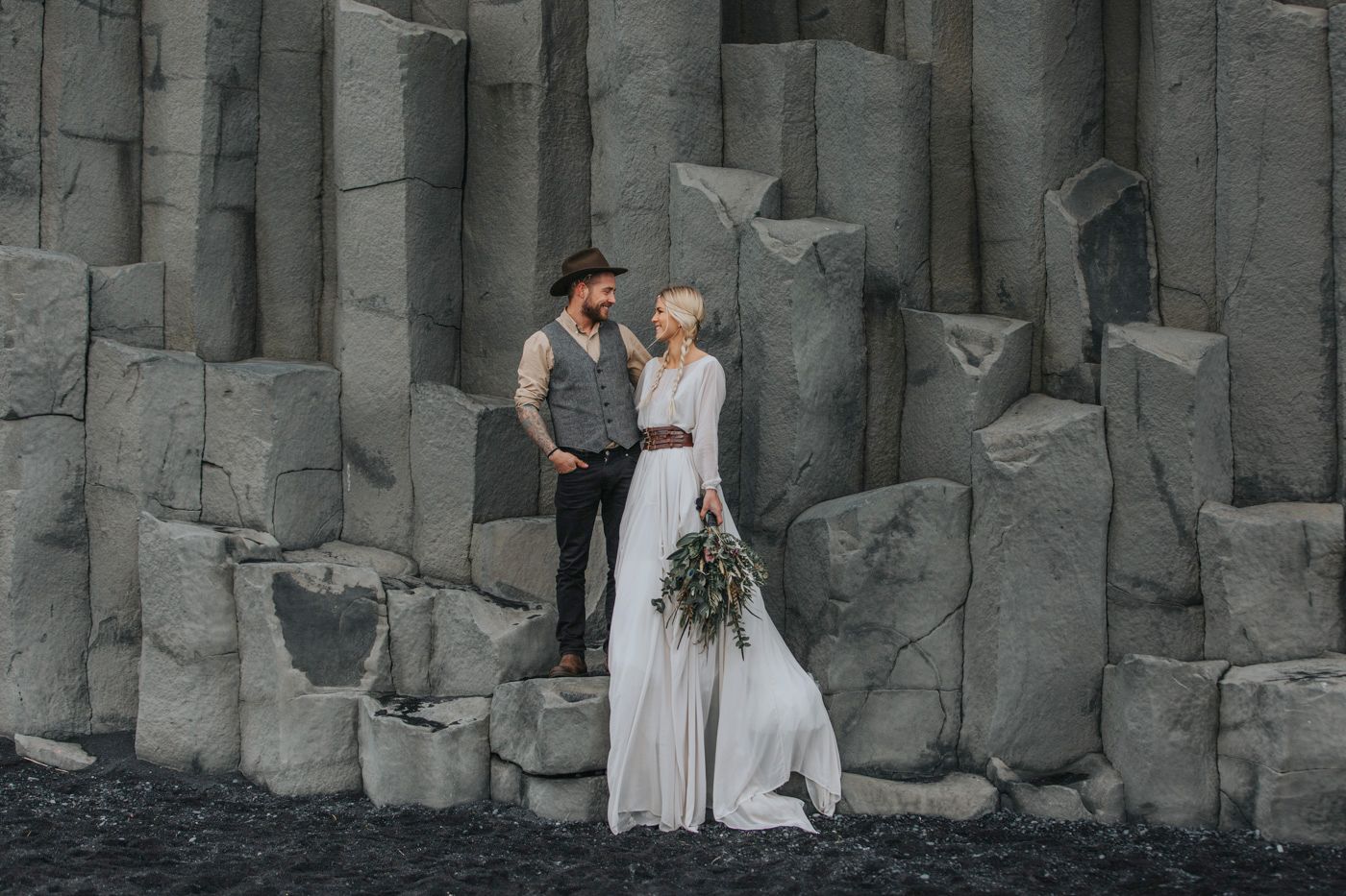An ethereal wedding portrait showcasing a flowing white dress against dark basalt cliffs.