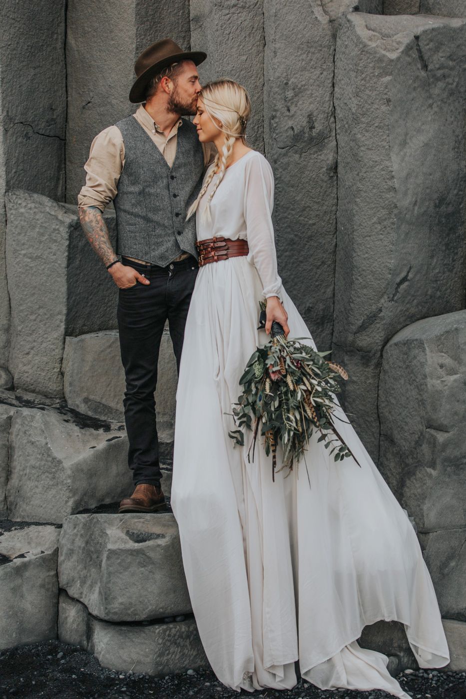 A romantic wedding photo featuring vintage-inspired fashion against dramatic volcanic rocks.