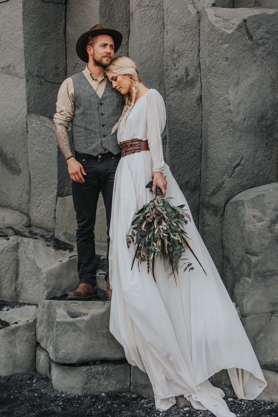 A couple in bohemian wedding attire standing on stone steps with a natural bouquet.