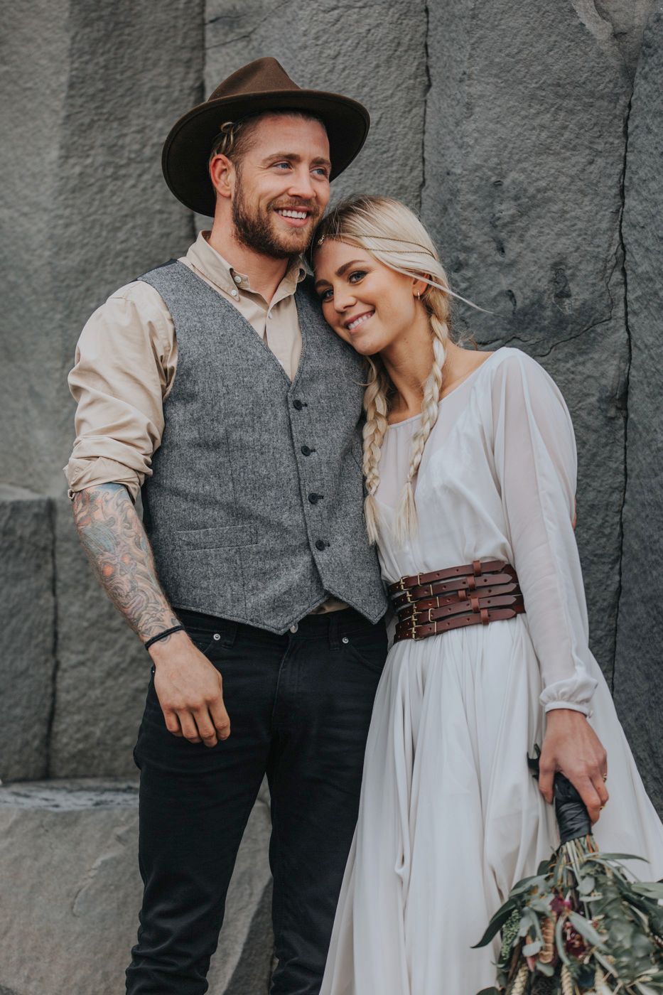 A couple shares an intimate moment in vintage-inspired wedding attire against a stone backdrop.
