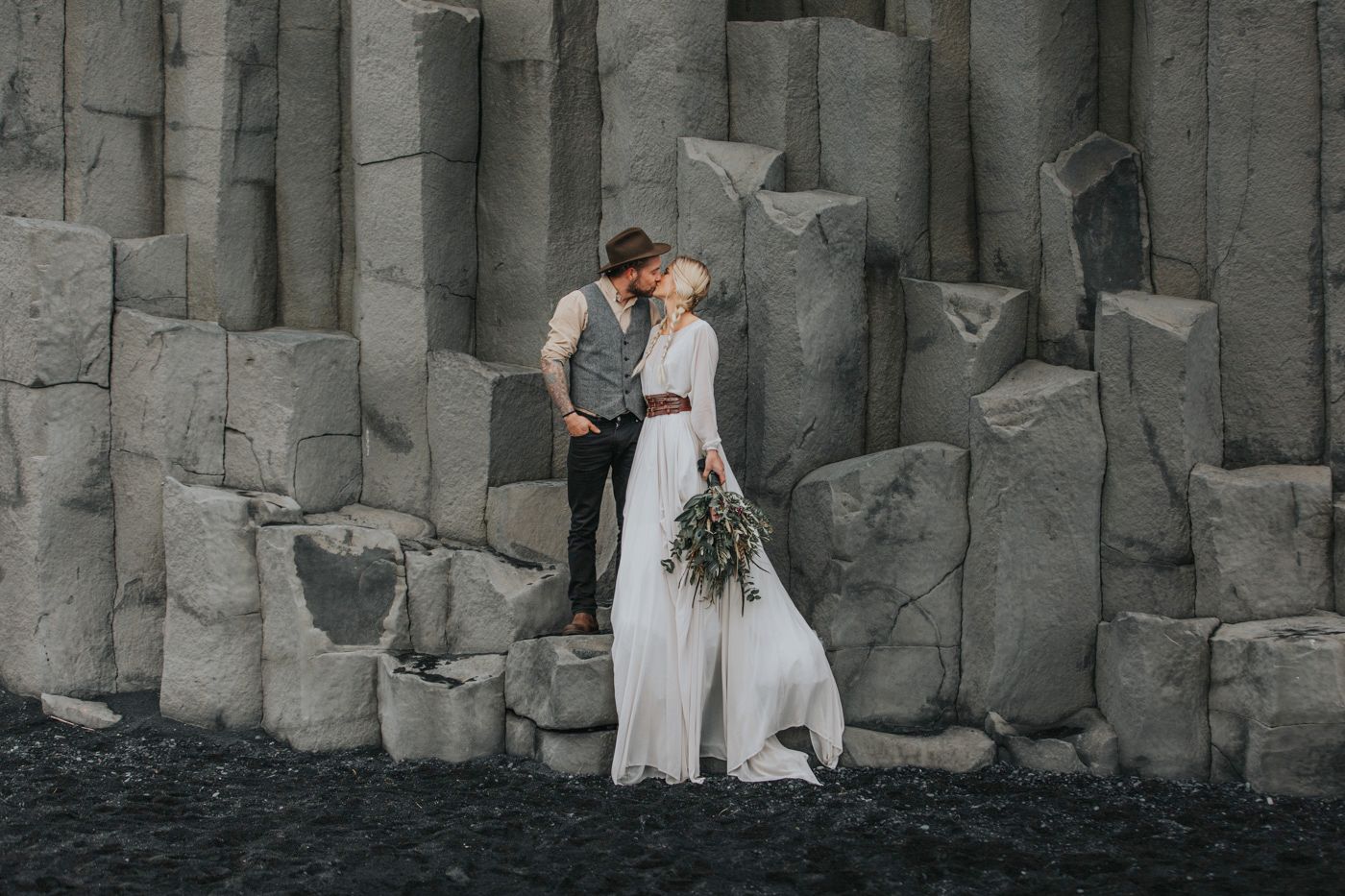 A wedding couple embraces among dramatic basalt columns on a volcanic beach.