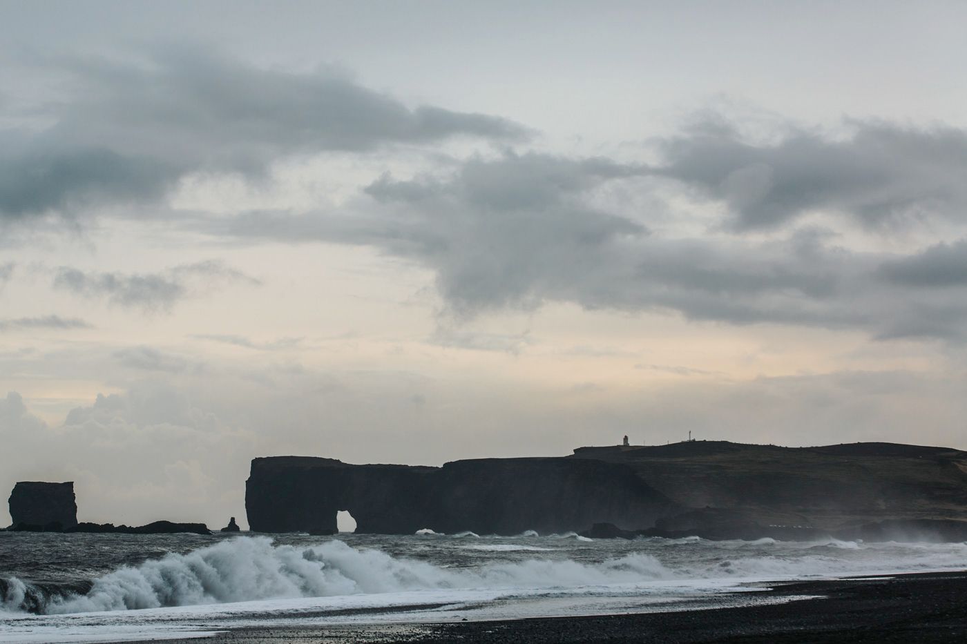 Dramatic coastal cliffs and crashing waves under a moody sky in Iceland.