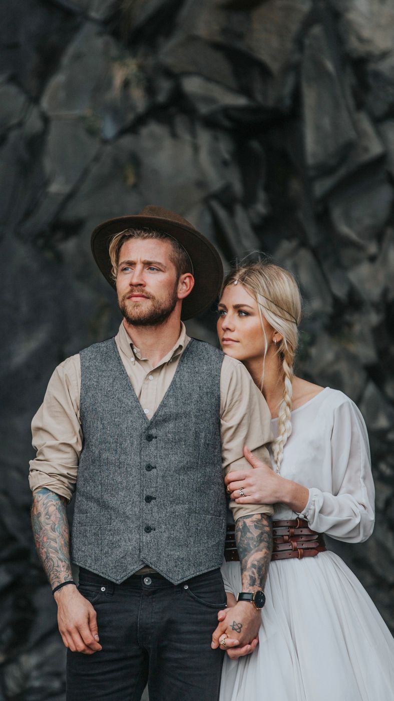 Intimate wedding portrait against dark volcanic cliffs showing rustic western style attire.