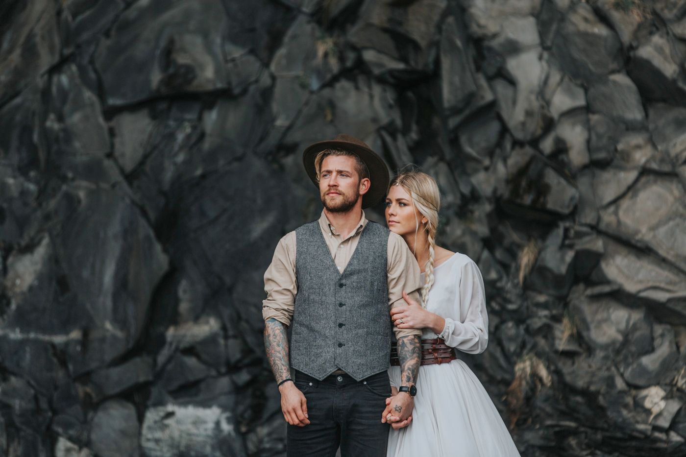 Rustic wedding portrait showing western style groom's attire against volcanic cliff backdrop.