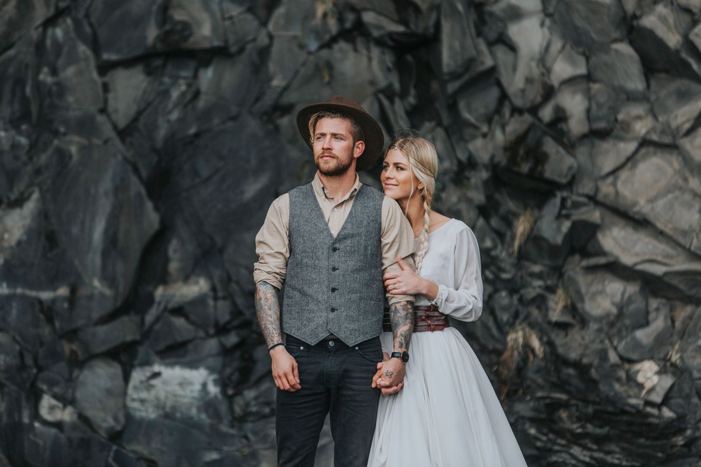 Moody wedding photography with couple against dramatic dark rock formations.
