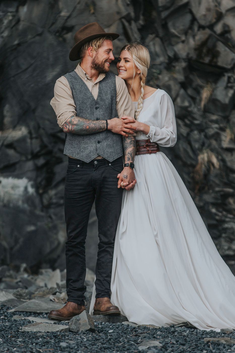 Joyful wedding moment captured against textured dark cliff face.