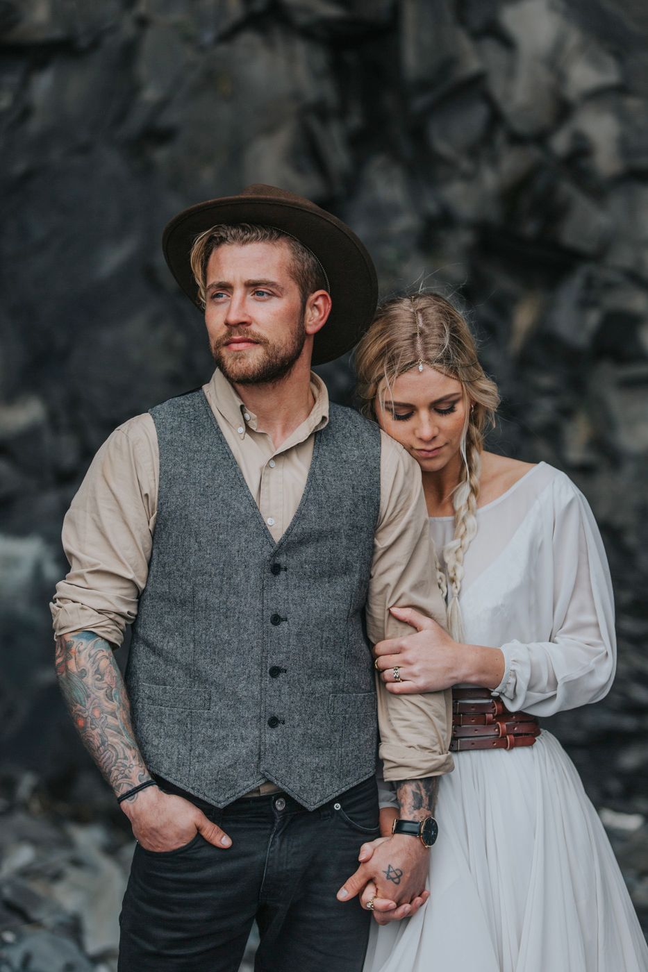 Intimate portrait of couple in vintage-inspired wedding attire against dark stone backdrop.