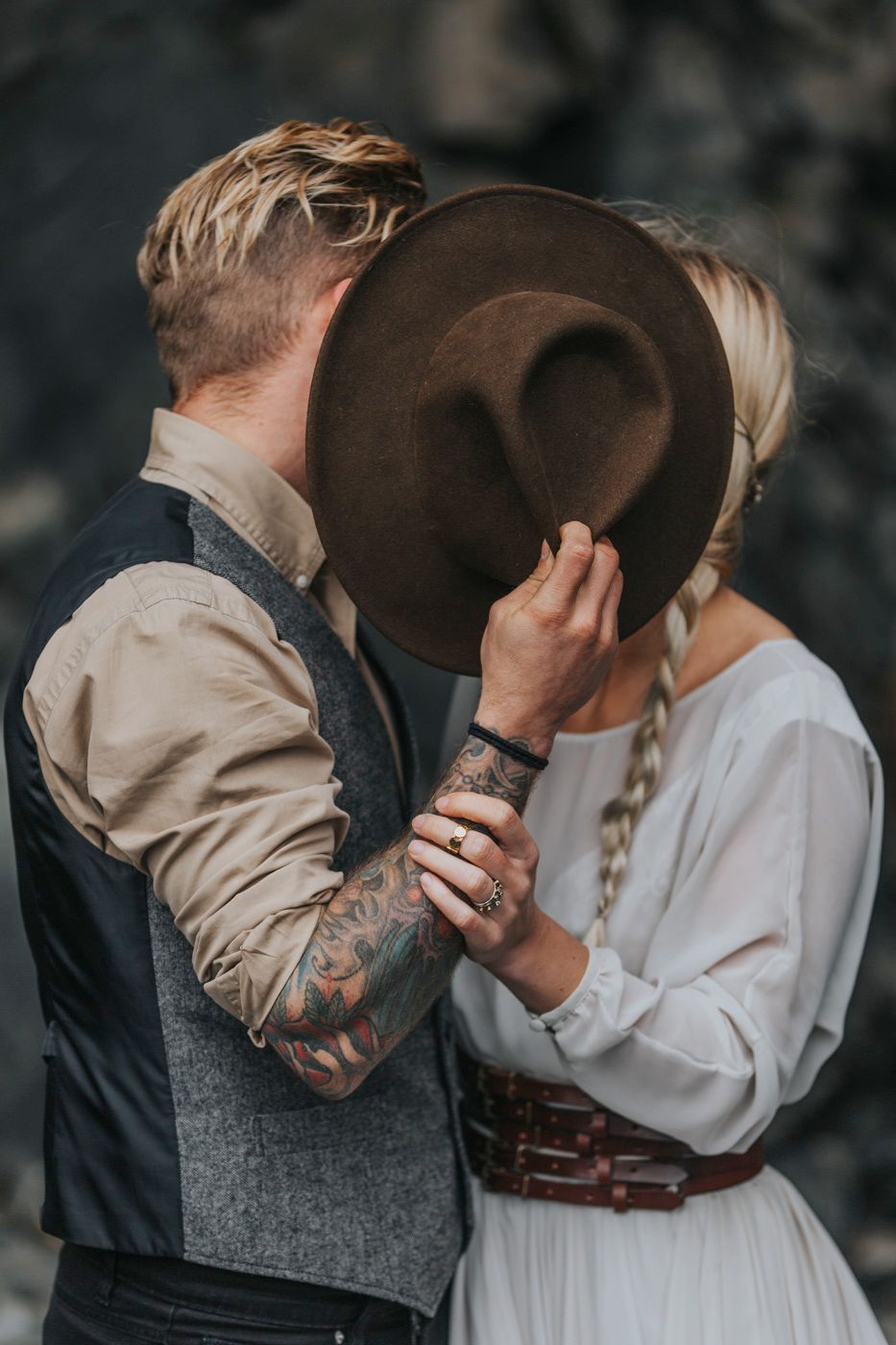 Romantic moment between couple sharing kiss behind brown fedora hat.