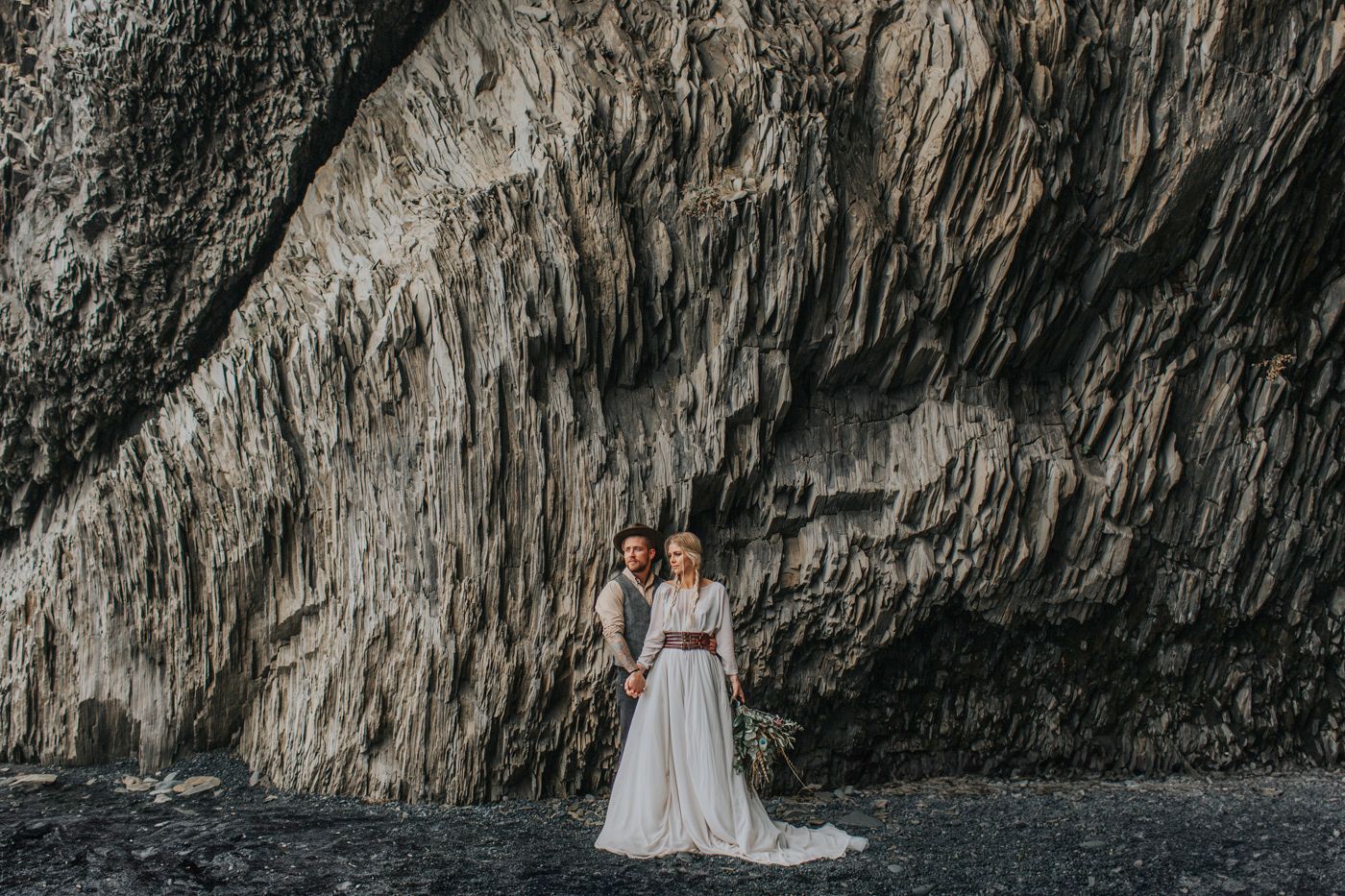 Distant shot of wedding couple against towering textured rock formation.