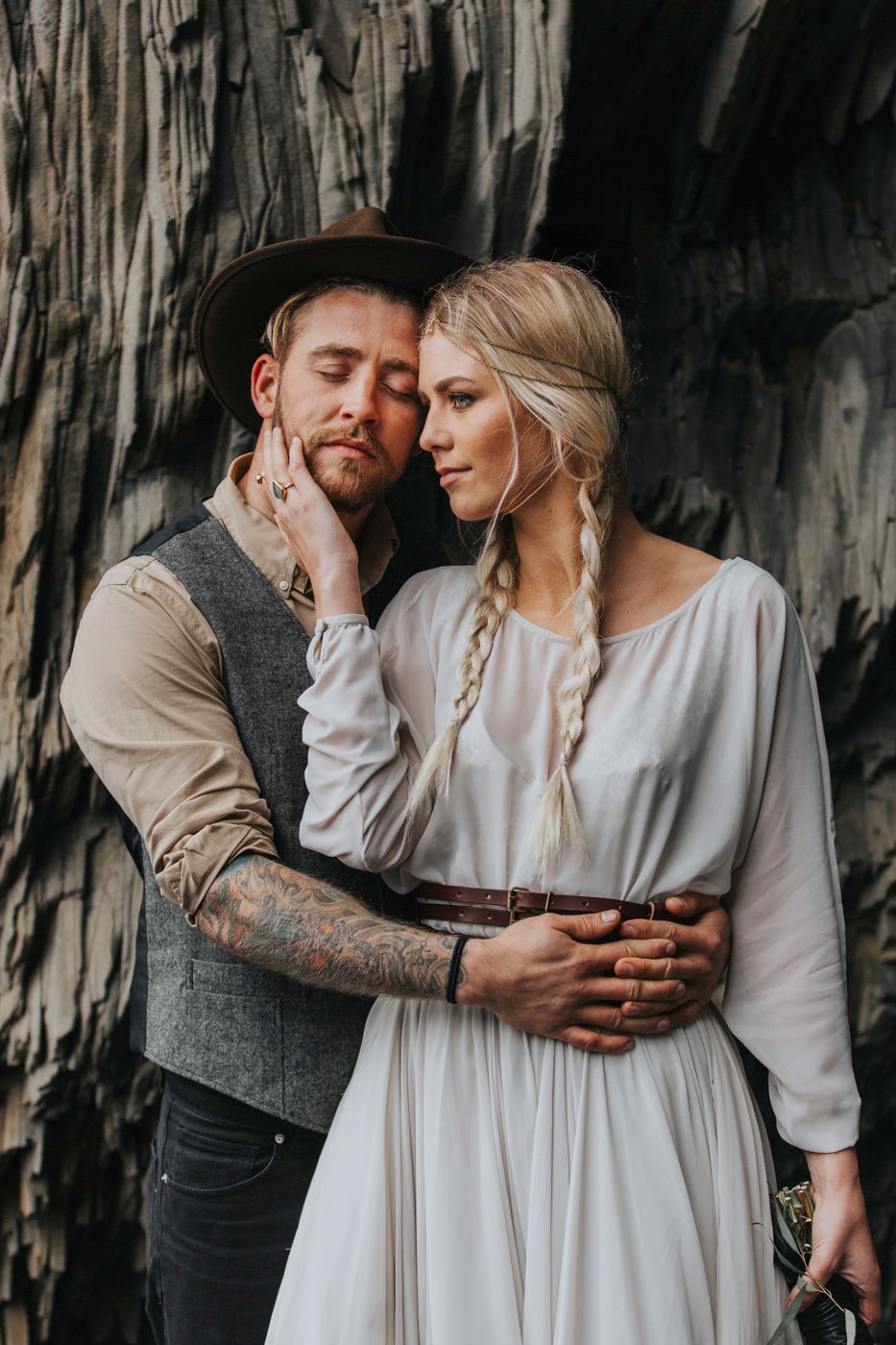 Intimate moment between couple in vintage wedding attire against textured stone wall.