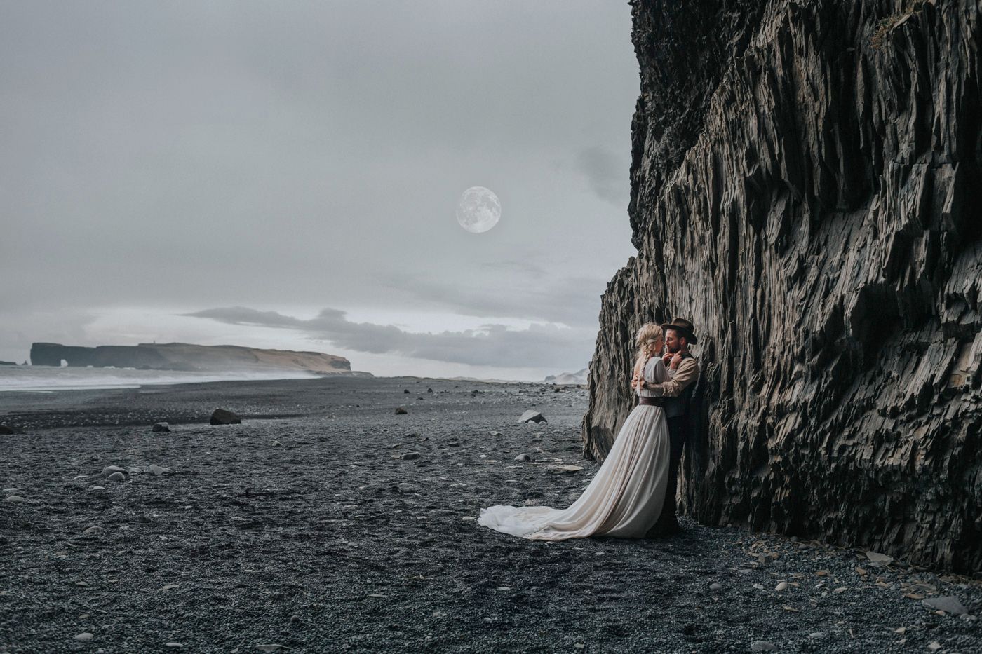 Dramatic wedding photo against black cliffs and moody sky with visible moon.