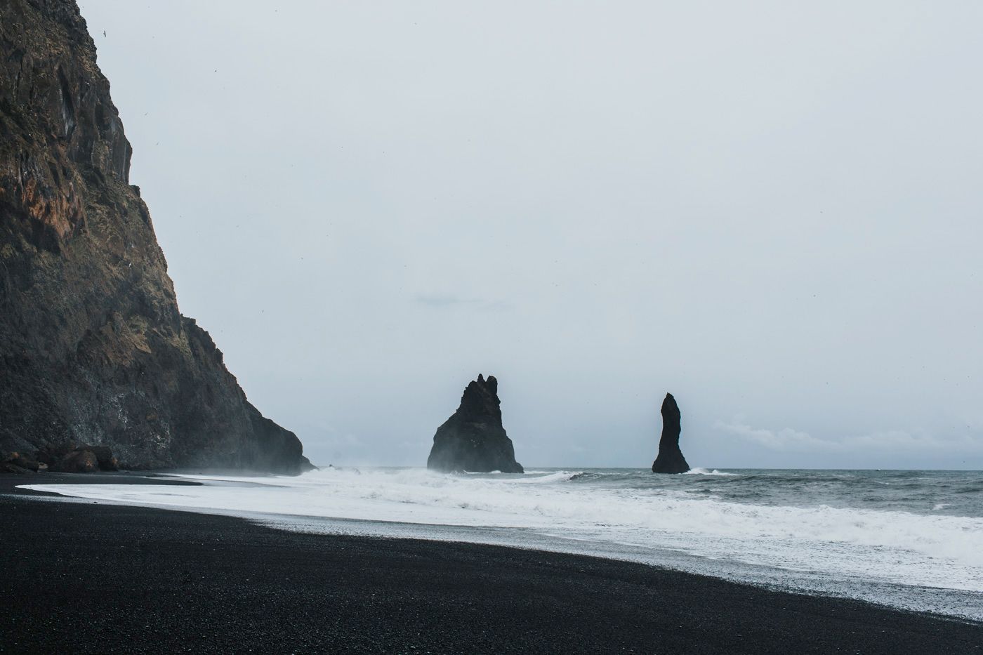 Dramatic black sand beach with towering sea stacks and misty coastline.