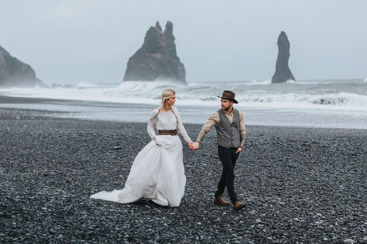 Wedding couple strolling along Iceland's iconic black sand beach with sea stacks.