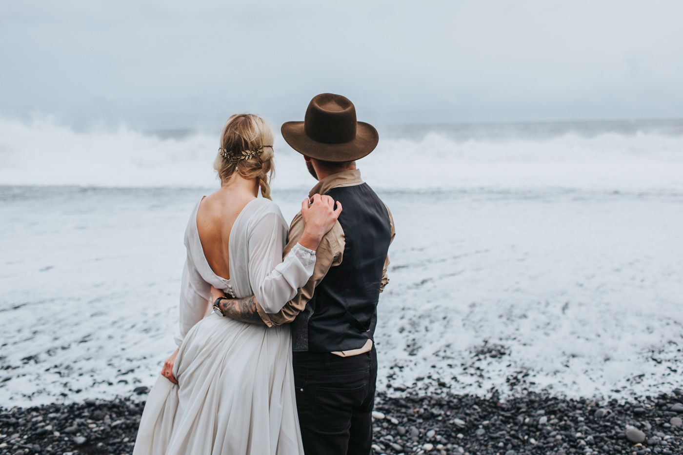 Intimate moment between newlyweds on moody black sand beach.