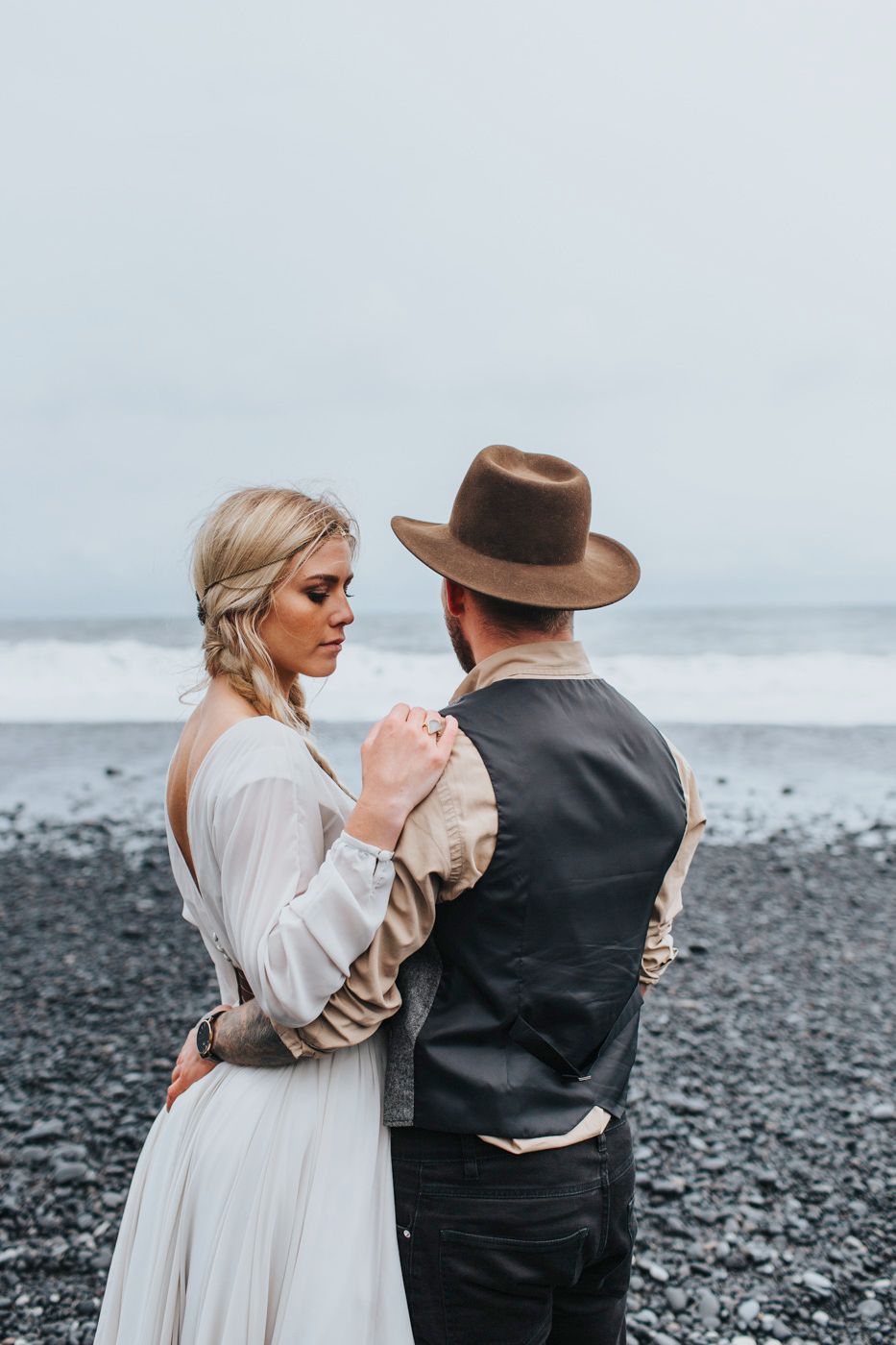 Romantic couple embraces on a moody black sand beach with ocean waves in the background during a wedding photoshoot.