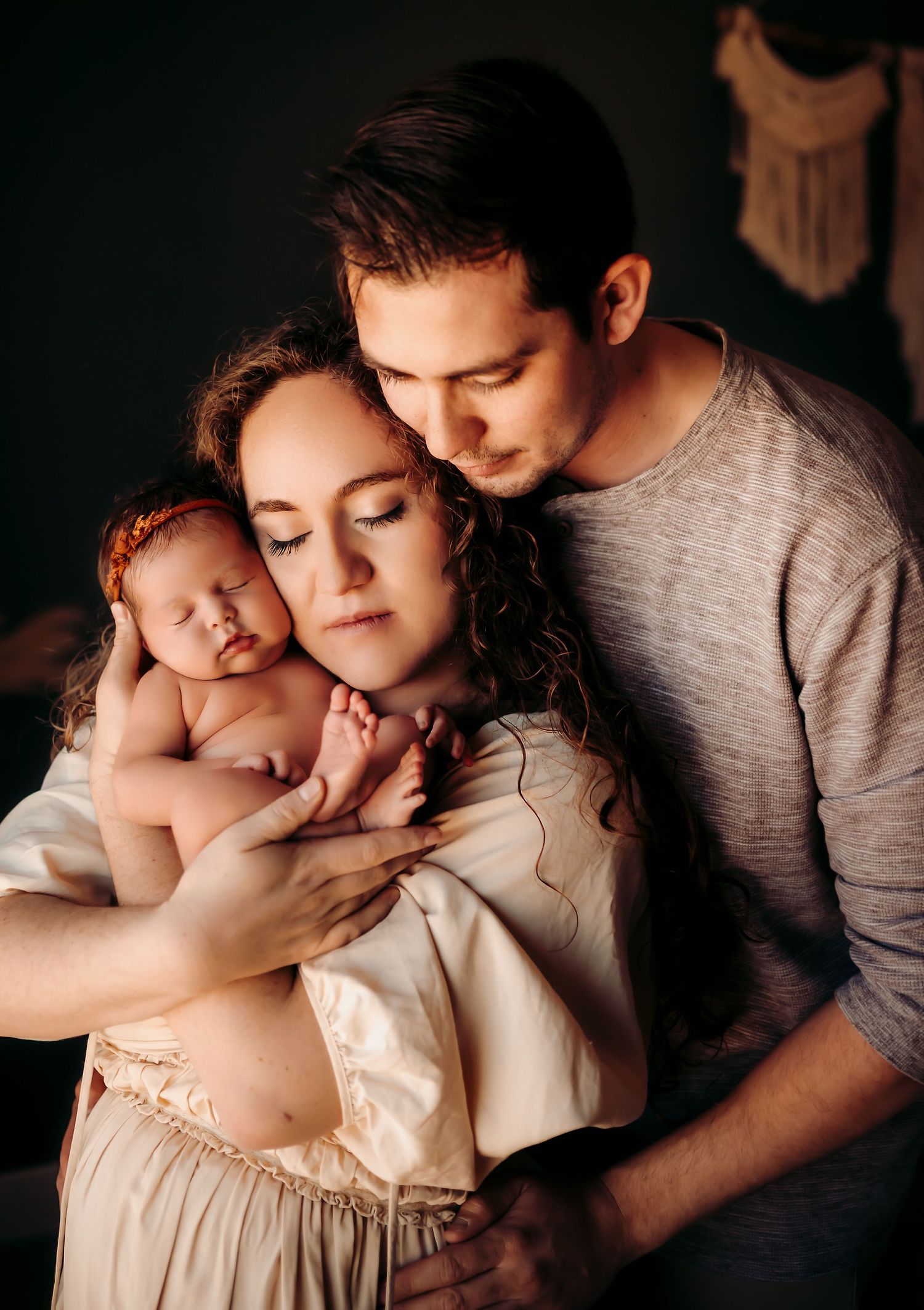 An intimate family portrait shows tender moment as parents cradle their newborn baby in soft natural lighting.