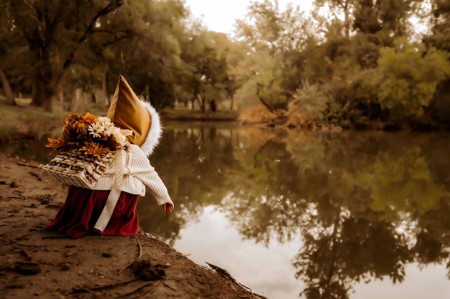 Decorative fox doll sitting by reflective pond in autumn setting.