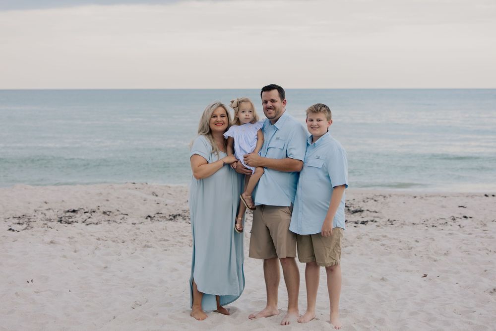 Happy family of four posing together on sandy beach with ocean waves in background.