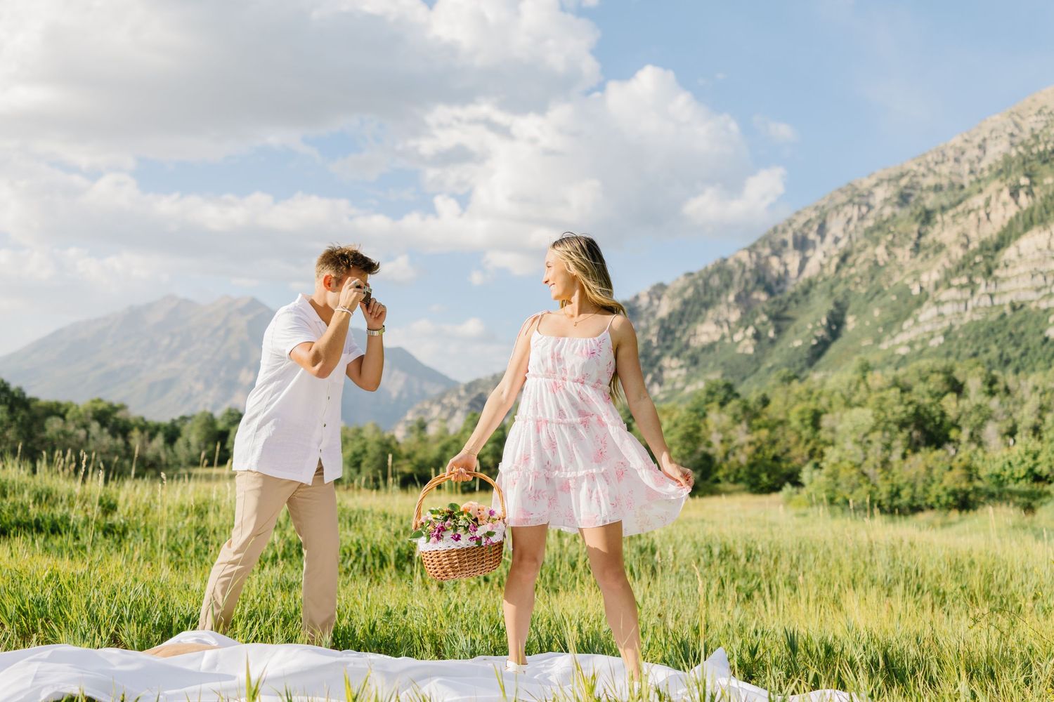 Two people having picnic on blanket in mountain meadow with wildflowers.
