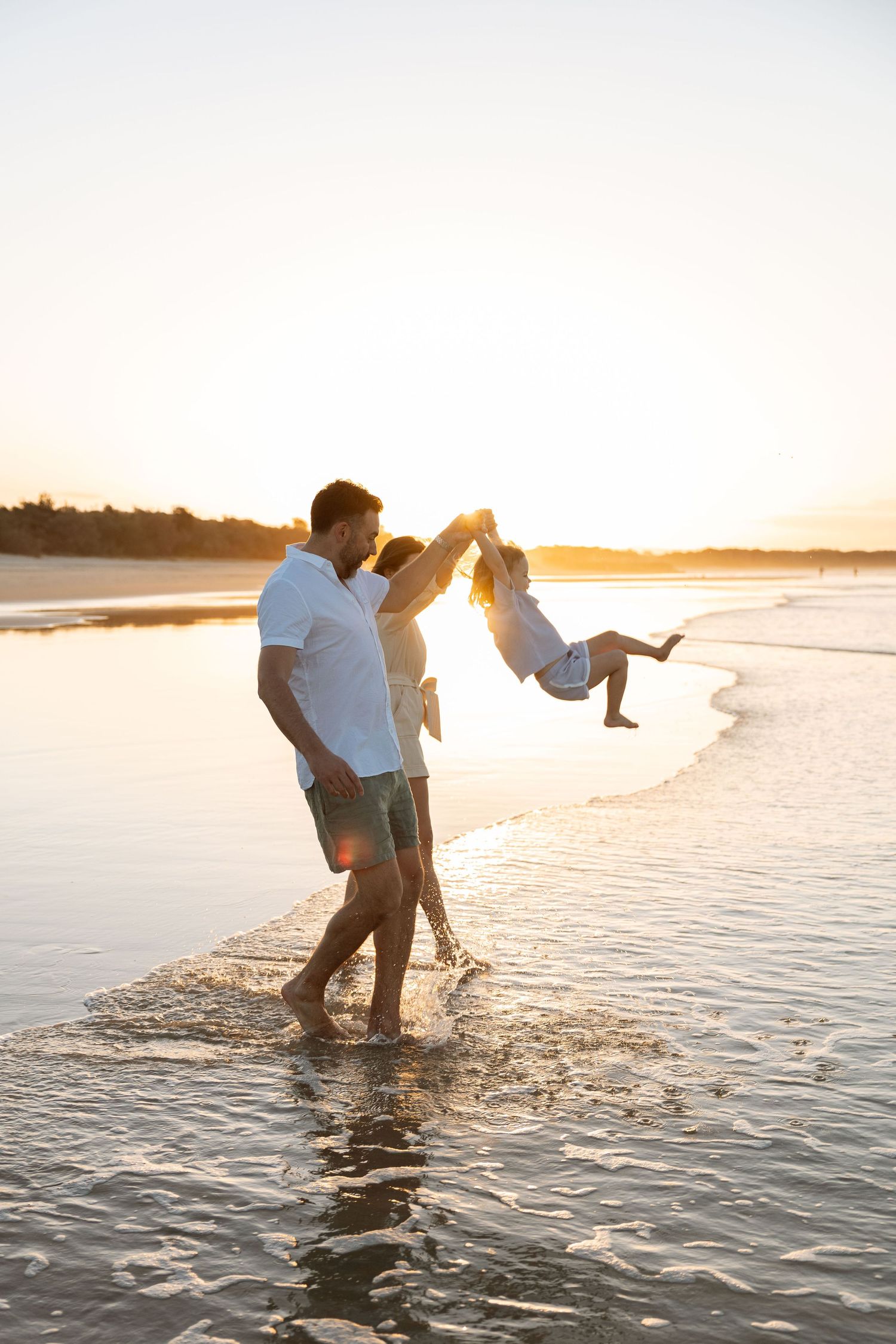 A family having fun at the beach in sunset. A beautiful moment of Mum and Dad swinging their daughter in the sunset.