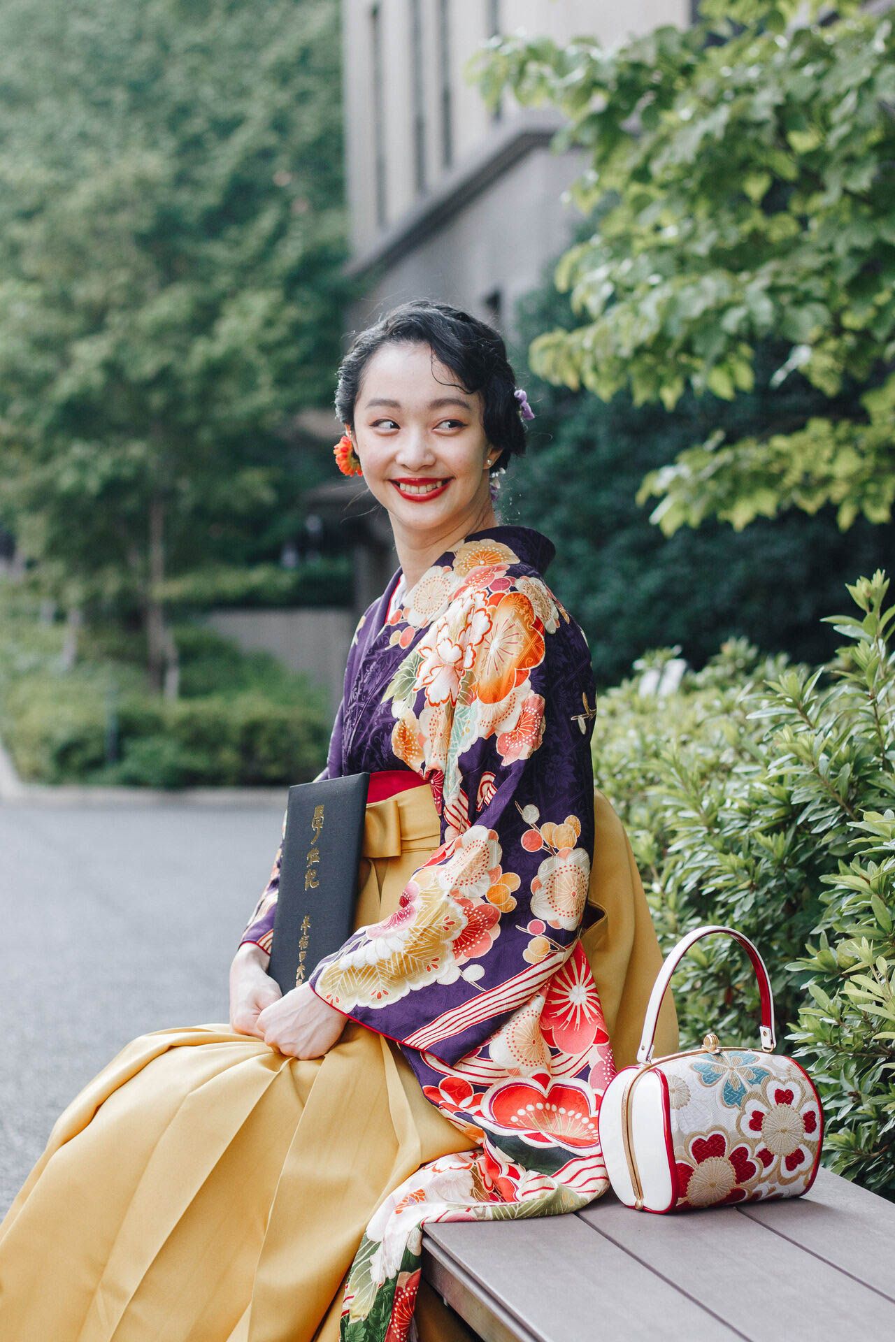 A woman in a colorful kimono sits with graduation diploma and traditional accessories.